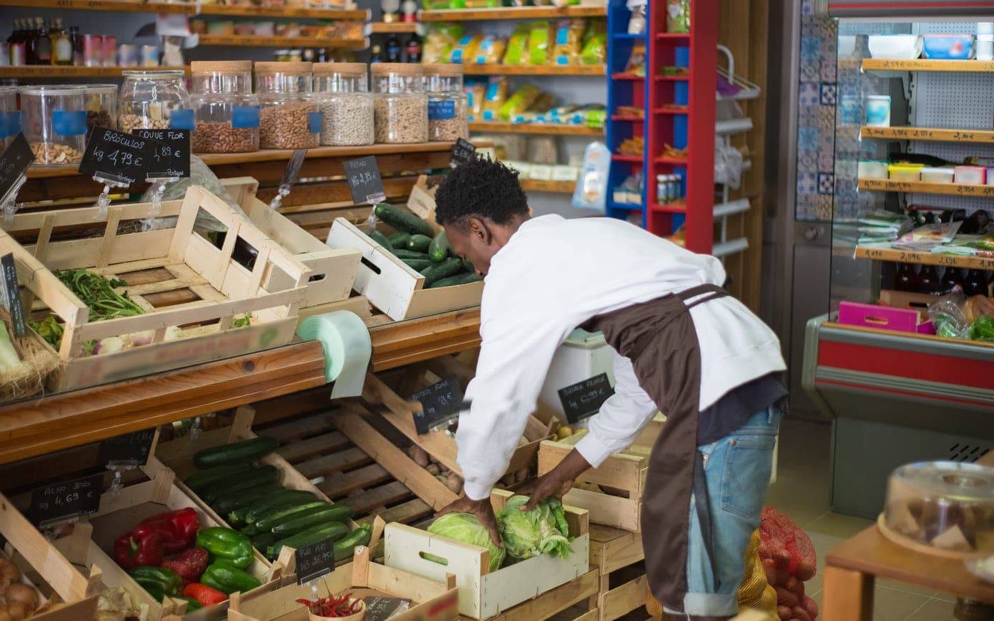 A shopkeeper restocking the vegetable shelves